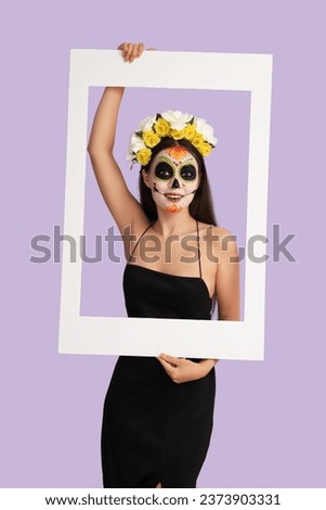 Young woman with painted skull and frame on lilac background. Mexico's Day of the Dead (El Dia de Muertos) celebration