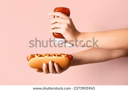Woman adding ketchup onto tasty hot dog on pink background Royalty-Free Stock Photo #2373905965