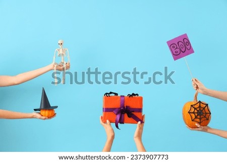Women with Halloween gifts, pumpkins and decor on blue background