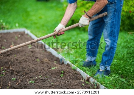 Farmer cultivating land in the garden with hand tools. Soil loosening. Gardening concept. Agricultural work on the plantation. Royalty-Free Stock Photo #2373911201