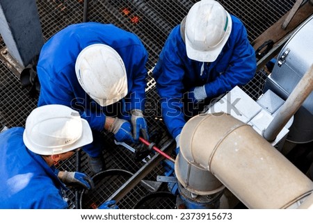 A group of mechanic wearing blue clothes, white helmets and personal protective equipment are assembling a flange at a piping system Royalty-Free Stock Photo #2373915673