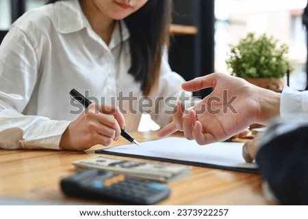 Young woman checking agreement before signing while sitting at the financial advisor office.