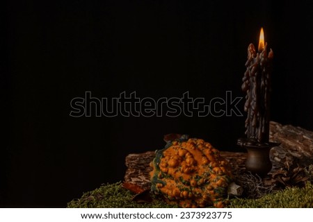 View of a black candle burning in antique candlestick, on table with pumpkin and autumn leaves, black background, horizontal, with copy space