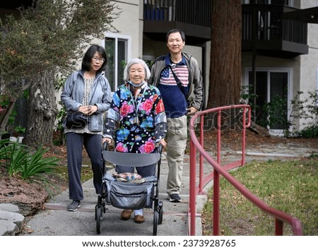 Senior woman with facemask under her chin, walking with family in the courtyard of retirement home. California.