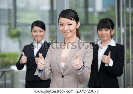 Asian businessman and businesswoman with thumbs up outside office.