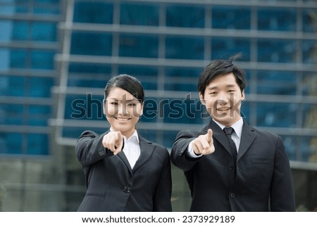 Asian business man and woman pointing at the viewer.
