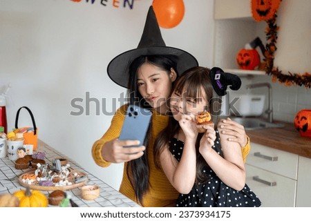 A cute and happy young Asian girl in a Halloween costume is taking selfies with her mom, celebrating Halloween at home together.
