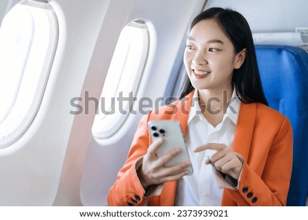 Smiling Asian woman enjoying her comfortable flight while sitting in the airplane cabin, wifi internet on the plane. Passengers near the window.