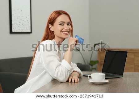 Happy woman with credit card near laptop at wooden table in room. Online shopping