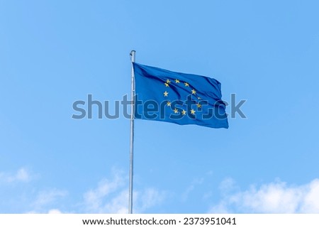 The flag of the European Union on the flagpole develops in the wind against the blue sky