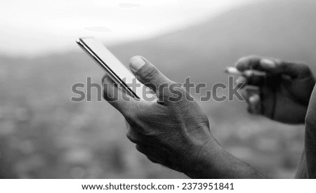 Person using phone. Hands of a business man holding cigarette while checking cellphone outdoor in black and white background.