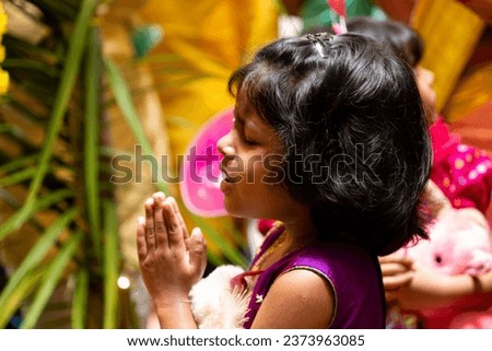 A young girl praying with her hands folded together.