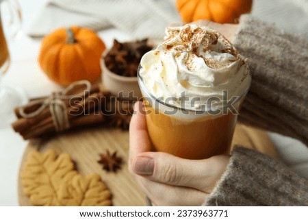 Woman holding cup of tasty pumpkin spice latte with whipped cream at white table, closeup