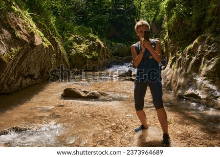 Woman tourist with backpack taking photos with her phone in a gorge