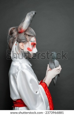 Beautiful woman in animal mask holding bird pigeon on black background. Halloween, Carnival and Cosplay concept