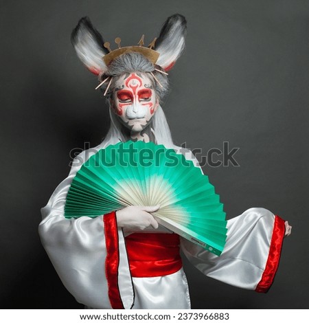 Beautiful woman in animal mask holding green fun on black background. Halloween, Carnival and Cosplay concept