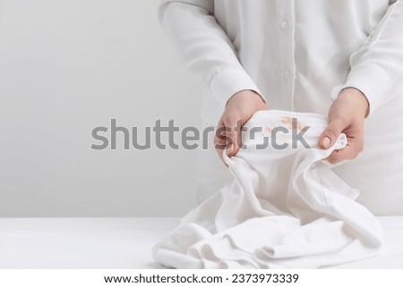 Woman holding shirt with stain at table against light background, closeup. Space for text Royalty-Free Stock Photo #2373973339