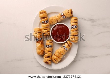 Plate with tasty sausage mummies for Halloween party and ketchup on white marble table, top view