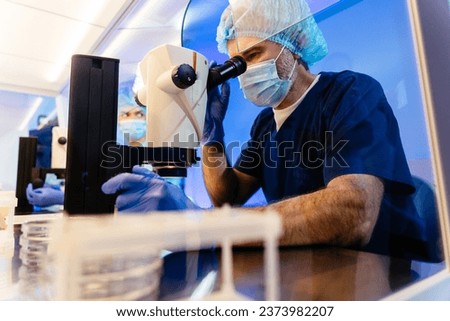Modern medical research laboratory. Mature male scientists in protective wear working, using Inverted microscope, analyzing test, talking.