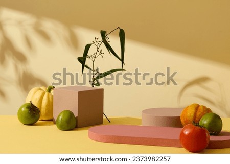 Autumn floral frame with pumpkin, tomato, green persimmon and leaves branch decorated with empty podiums on yellow background. Front view, advertising photo with blank space