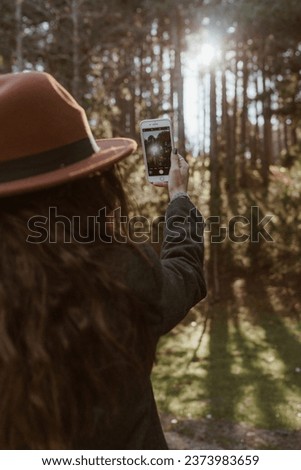 a woman holds an iphone and shooting forest photo ligh leaking between trees sunset sunrise shadows golden hour