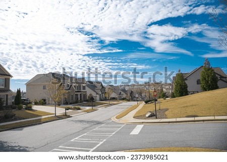 Three-way road intersection with stop sign, row new development suburban two story houses along street leading down steep hill near Atlanta, Georgia, USA, well-trimmed landscape. Sunny cloud blue sky