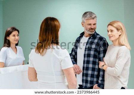 Medical staff and nurse. Receptionist talking to couple patients in front of reception counter in hospital. Mature man woman having conversation at reception. Family, wellness infertility consultation