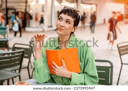 woman student writing in a notebook, making a plan at the street cafe in city. Concept of study hard Lifestyle photo Royalty-Free Stock Photo #2373995947