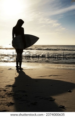 Silhouette, woman surfer on beach sand and ocean, exercise outdoor and healthy with surfboard and scenic sea view. Sports, shadow and sun with female person in nature and ready to surf for fitness Royalty-Free Stock Photo #2374000635