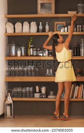 A young woman reaching up to get something from a shelf. Short female on the tiptoes taking an object of a high cupboard. Lady with a small stature stretching her arm to retrieve an item Royalty-Free Stock Photo #2374001035