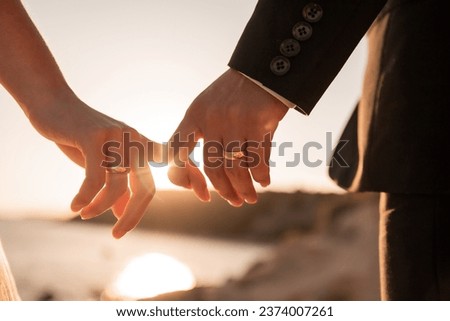 romantic couple holding hands fingers at sunset leaking wedding rings sunset rays bride groom wedding love couple golden hour  Royalty-Free Stock Photo #2374007261
