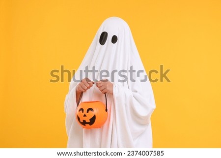 Woman in white ghost costume holding pumpkin bucket on yellow background. Halloween celebration Royalty-Free Stock Photo #2374007585