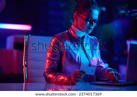Neon metaverse futuristic concept. trendy female in glasses with credit card using laptop in modern office.