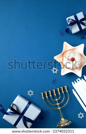 Hanukkah Jewish holiday vertical background with gold menorah, gift boxes, candles, traditional donut with jam on blue table. Flat lay, top view. Royalty-Free Stock Photo #2374032311