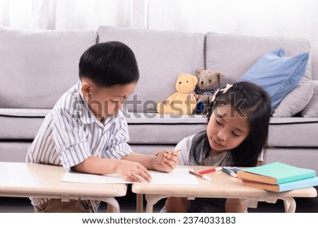 Two Asian siblings boy and girl having fun painting and drawing cartoons on paper in living room on holiday at home, family relationship childhood lifestyle playing together, school kids free time