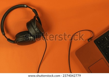Black headphones connected to laptop on orange background