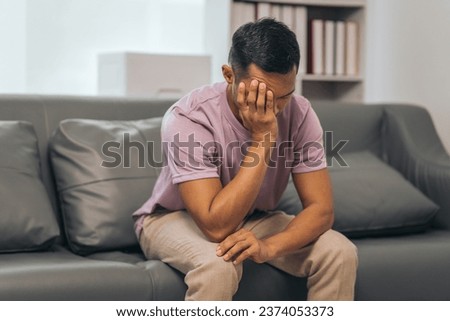 Middle-aged Asian Indian man with psychosis, depression, headache, migraine, sitting on sofa. Royalty-Free Stock Photo #2374053373