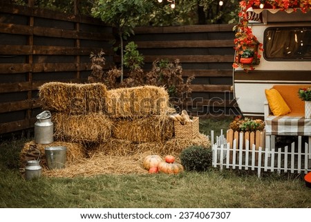 Camping season is autumn. Photo studio. Trailer against the backdrop of the forest. Pumpkins near the trailer, light bulbs glow, hay near the trailer, the sun is shining.