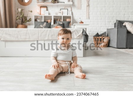 Portrait of a 7-9 month old baby in a home interior. A curious, smiling child explores the world around him. A cute baby is sitting on the floor. Royalty-Free Stock Photo #2374067465