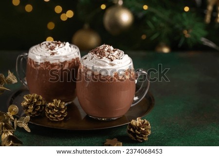 Hot chocolate with whipped cream in glass cups. Dark background with garland lights bokeh. Christmas and New Year sweet dfink and food holiday concept
