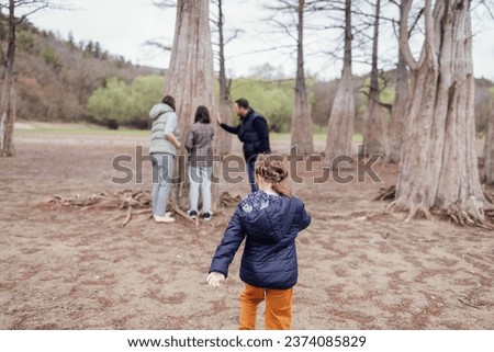 Happy family walks among huge cypress trees. Mom, dad and female teenager touch trunk of tree. Little cute girl runs to her parents and sister. Beautiful nature on background. Copy space.