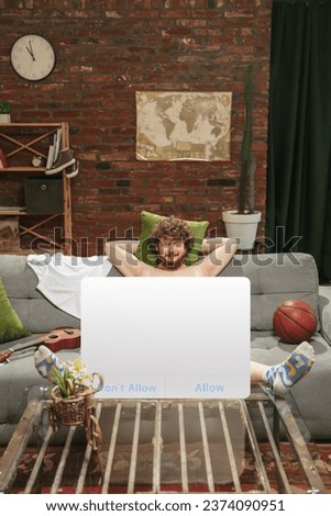 Portrait of young man with blank sign like social media screen sitting at home interior. Concept of confidentiality, private life, youth culture, human rights, facial expressions. Copy space for ad.