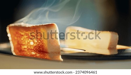 Two buttered croutons pop out of the toaster, steam emanating from the hot bread. The sun from the window illuminates the food beautifully Royalty-Free Stock Photo #2374096461