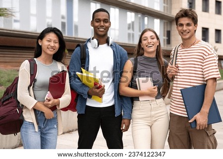 Portrait of multicultural group of happy students looking at camera with backpacks and notebooks. Diverse people smiling standing outside holding folders.