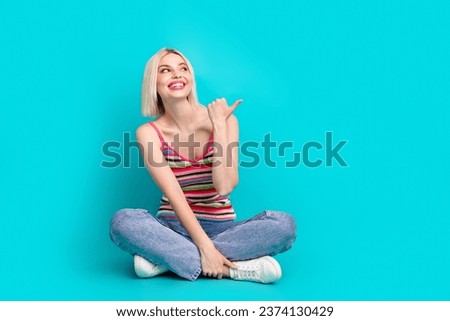 Full length photo of dreamy cute girl dressed striped tank top sitting legs crossed thumb empty space isolated teal color background