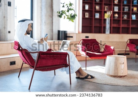 handsome man with dish dasha working in his business office of Dubai. Portraits of a successful businessman in traditional emirates white dress. Concept about middle eastern cultures. Royalty-Free Stock Photo #2374136783