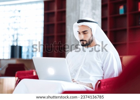 handsome man with dish dasha working in his business office of Dubai. Portraits of a successful businessman in traditional emirates white dress. Concept about middle eastern cultures. Royalty-Free Stock Photo #2374136785