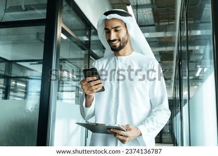 handsome man with dish dasha working in his business office of Dubai. Portraits of a successful businessman in traditional emirates white dress. Concept about middle eastern cultures. Royalty-Free Stock Photo #2374136787