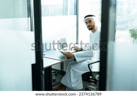 handsome man with dish dasha working in his business office of Dubai. Portraits of a successful businessman in traditional emirates white dress. Concept about middle eastern cultures. Royalty-Free Stock Photo #2374136789