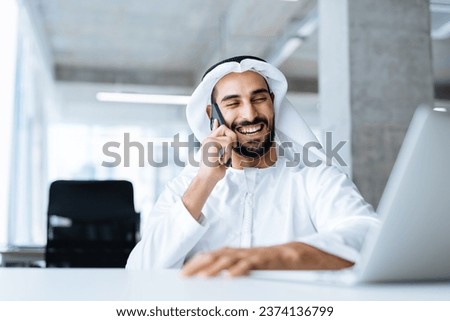 handsome man with dish dasha working in his business office of Dubai. Portraits of a successful businessman in traditional emirates white dress. Concept about middle eastern cultures. Royalty-Free Stock Photo #2374136799